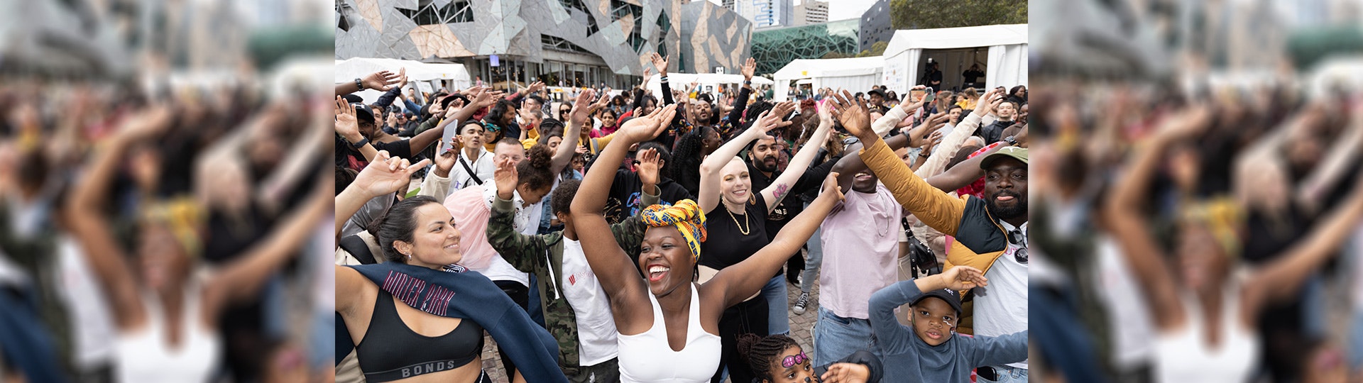 A group of people waving their arms and dancing during the African Music & Cultural Festival at Fed Square