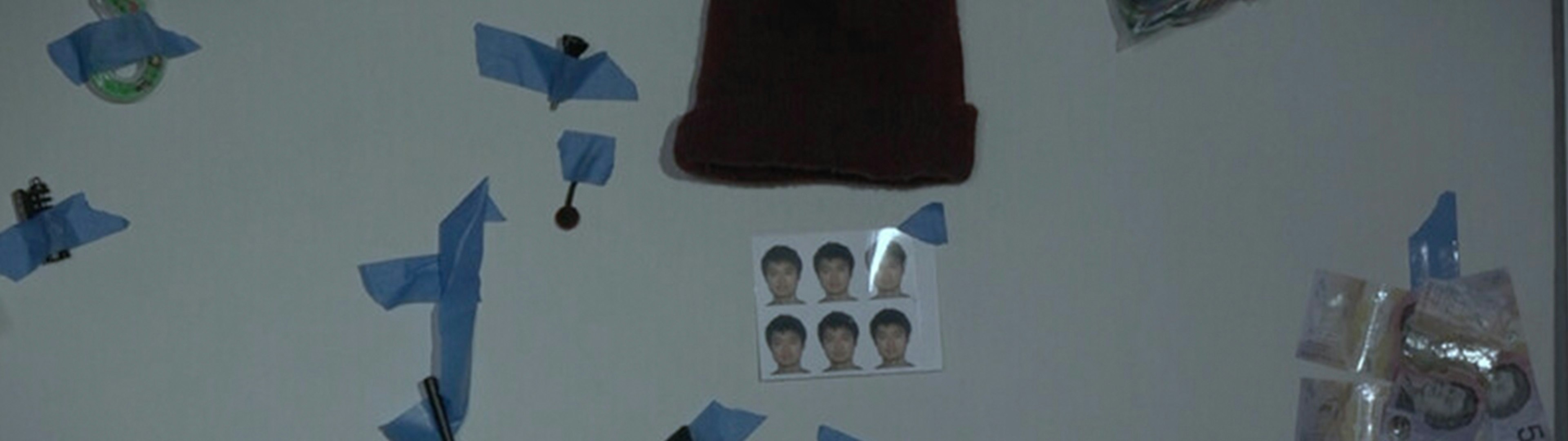 A passport photos, a black beanie, $5 notes and other odds and ends stuck to a wall with blue sticky tape