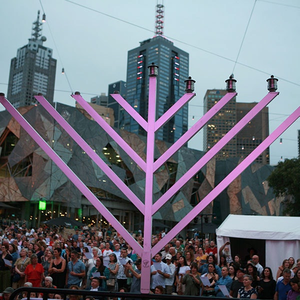 A close up on a menorah with Fed Square and a crowd in the background