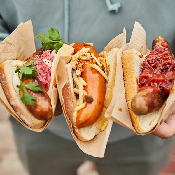 A close of a person holding three different gourmet sausages in bread with different toppings