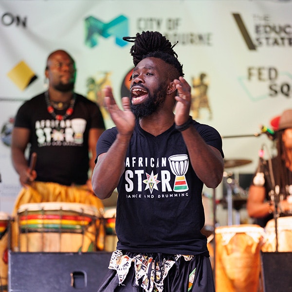 A man on stage wearing a black t-shirt with Africa Star written on it is mid clap while singing