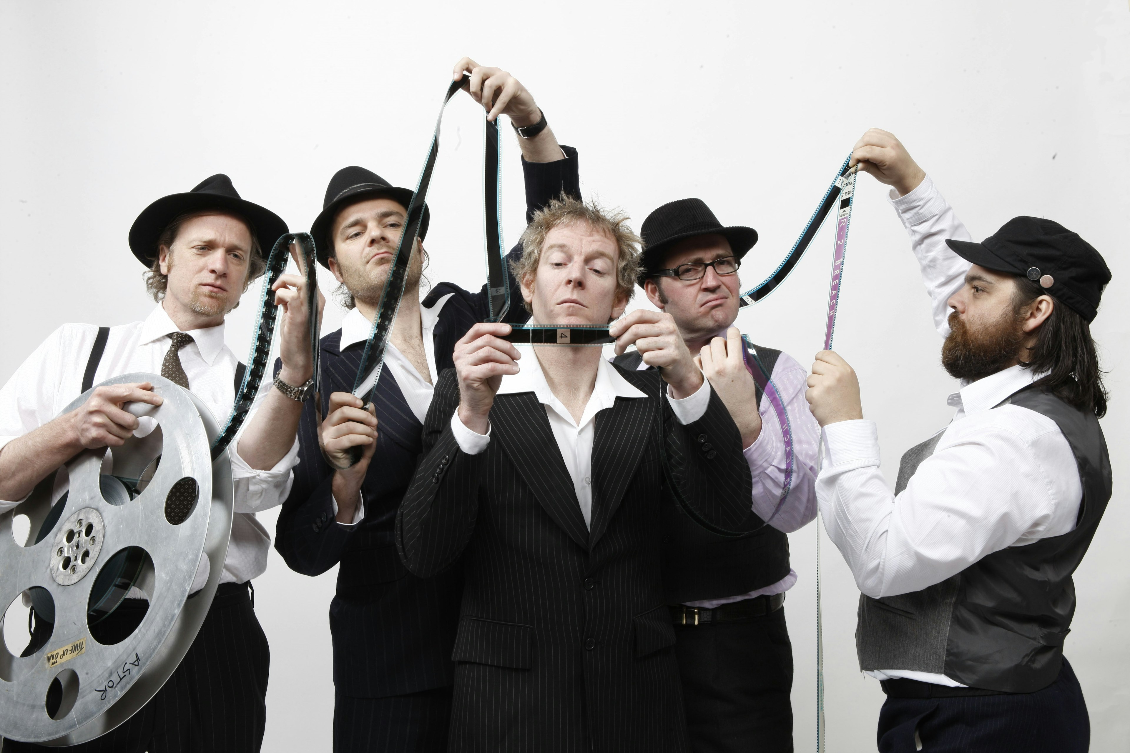 Five men, dressed in black and white shirts, ties and bowler hats, look quizzically at a reel of old-fashioned film. One of the men holds the huge reel under one arm, while the others inspect the tape that has come off the reel and is strung between them