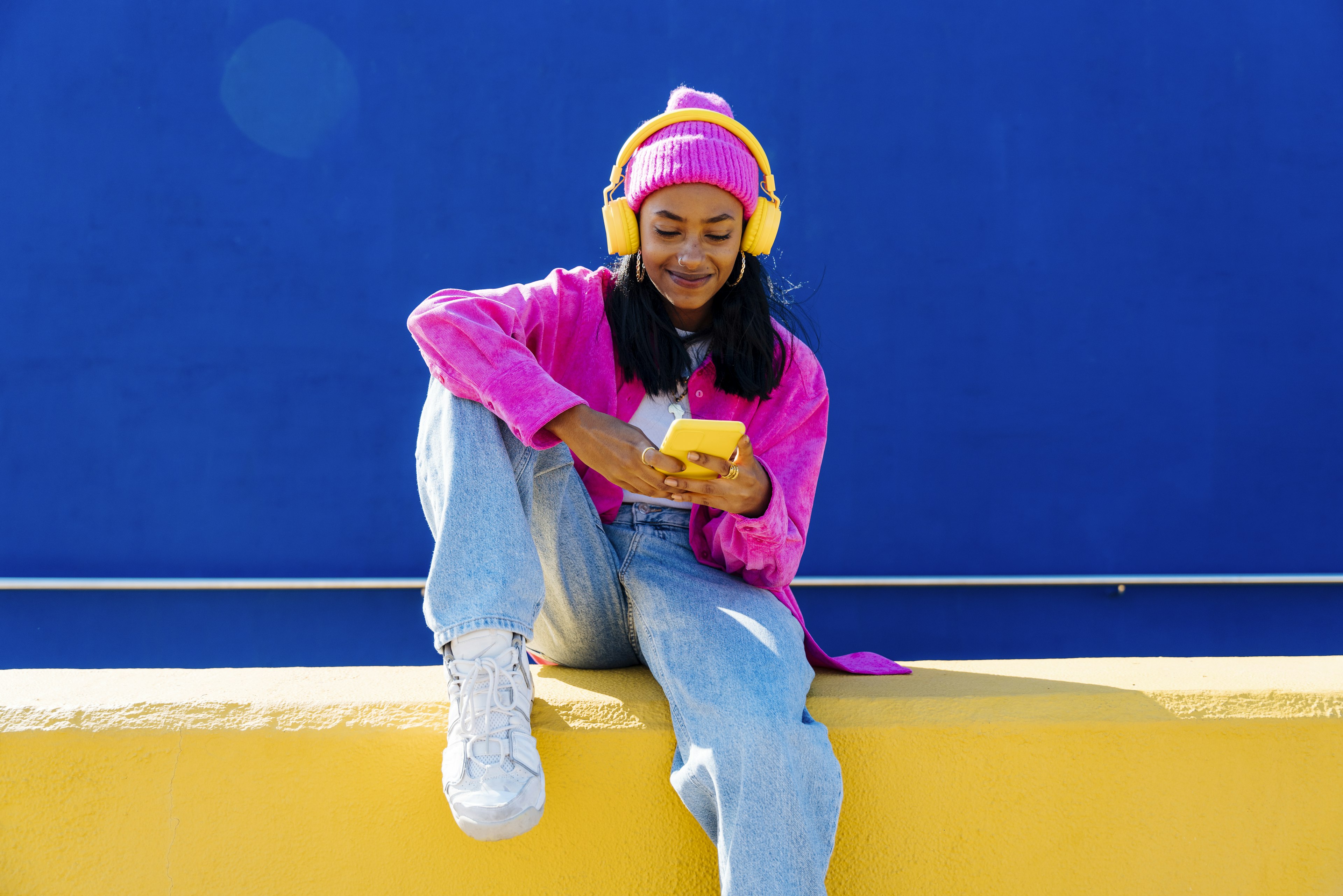 Smiling woman with headphones using smart phone on wall