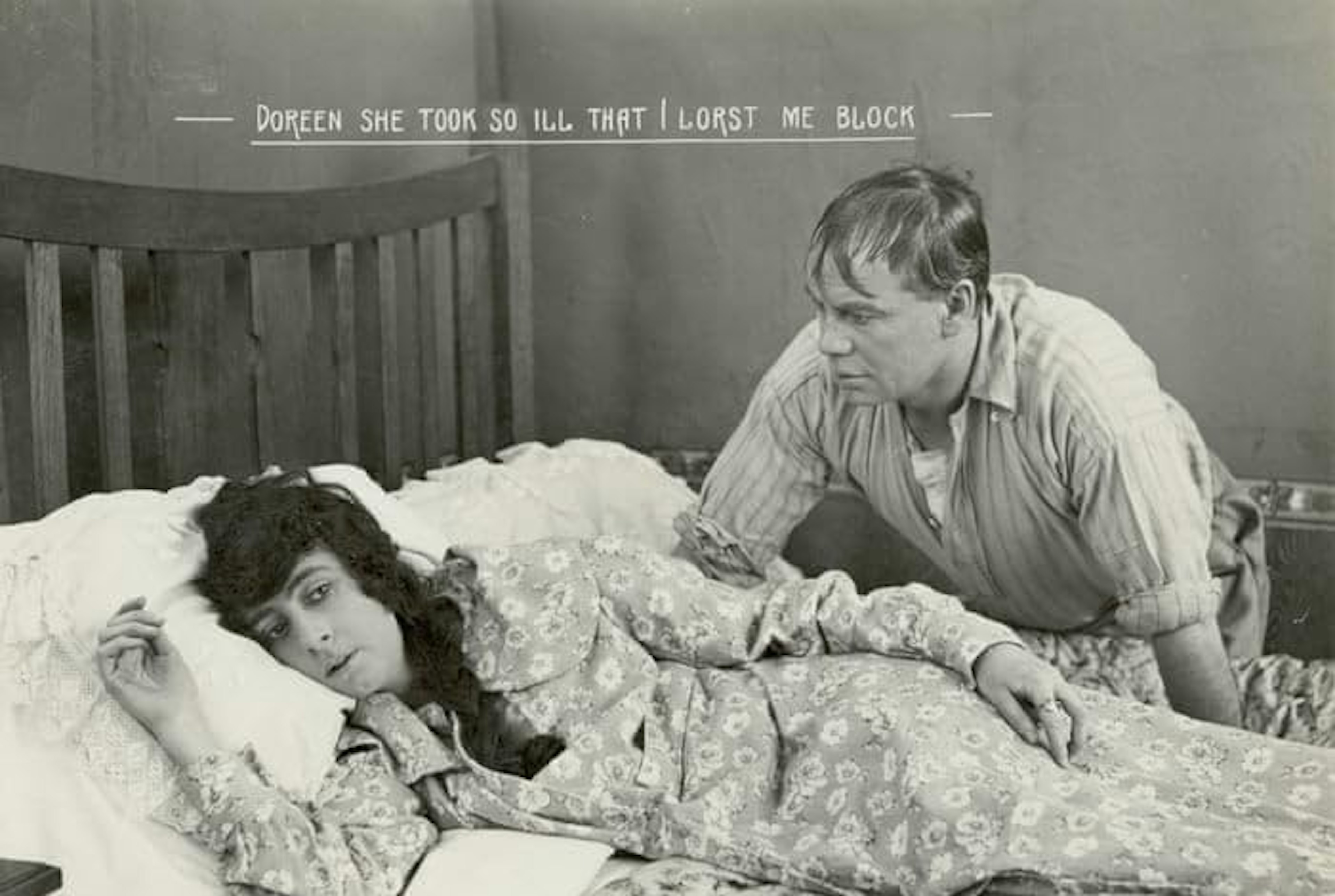 Film still from The Sentimental Bloke (1919). A woman with dark hair lies in a bed, and a man stands over her, looking at her. Card reads 'Dorren she took so ill that I lorst me block'