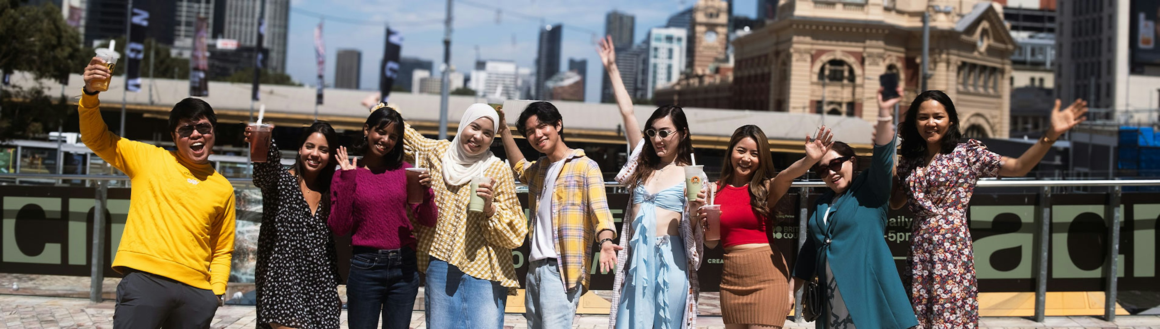 A group of young international students standing shoulder to shoulder smiling and posing for the camera at Fed Square