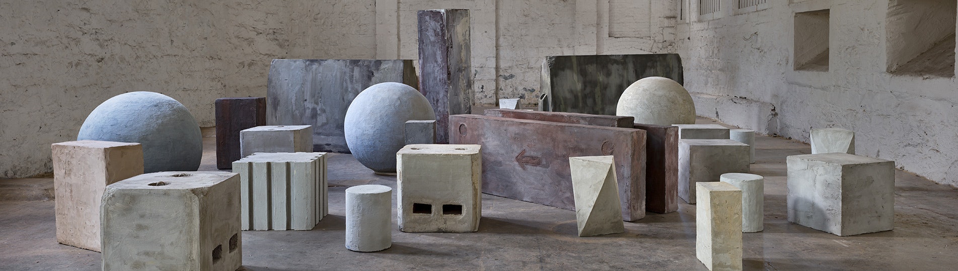 A photo of a collection of cement sculptures that are spheres, cubes and cuboids by artist Nina Sanadze