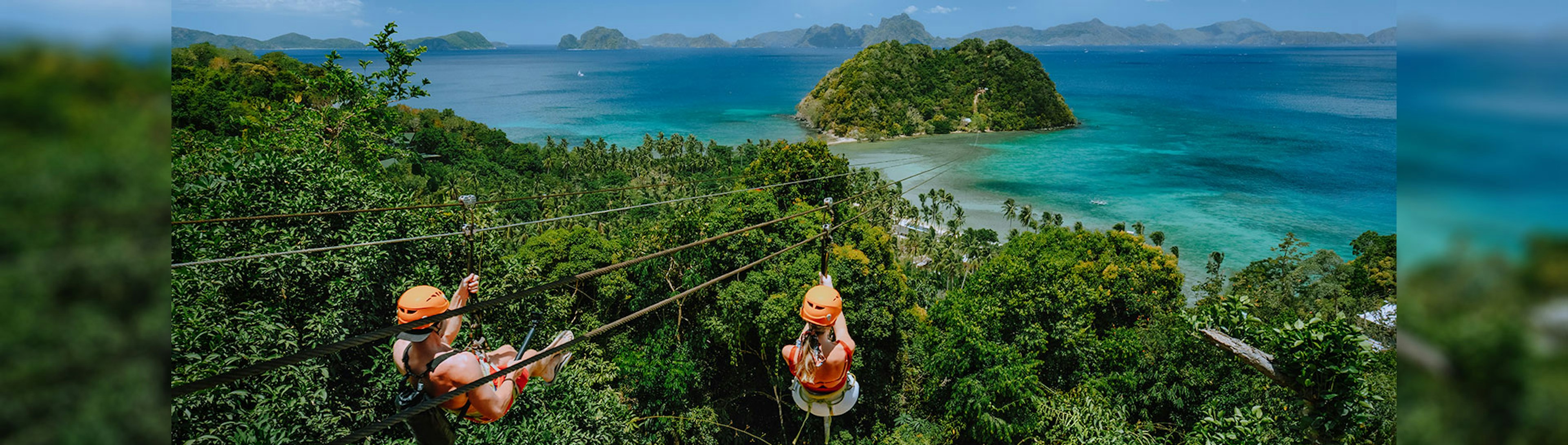 Two people ziplining over a jungle towards a small island over the coast in blue water in the Philippines