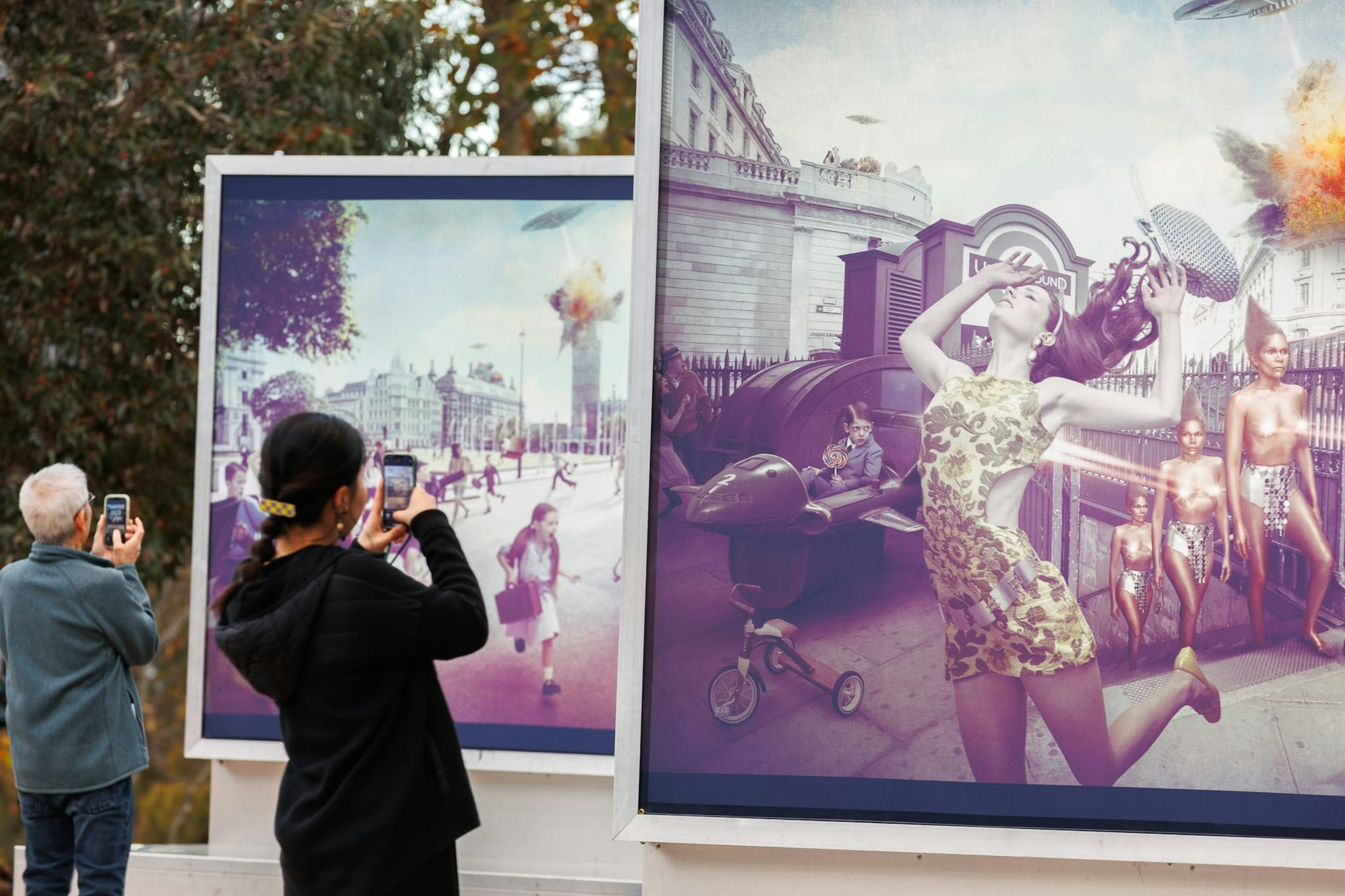 A man in a balck jumper takes a photo of a large lightbox depicting an image of a woman running away from a UFO in a British street