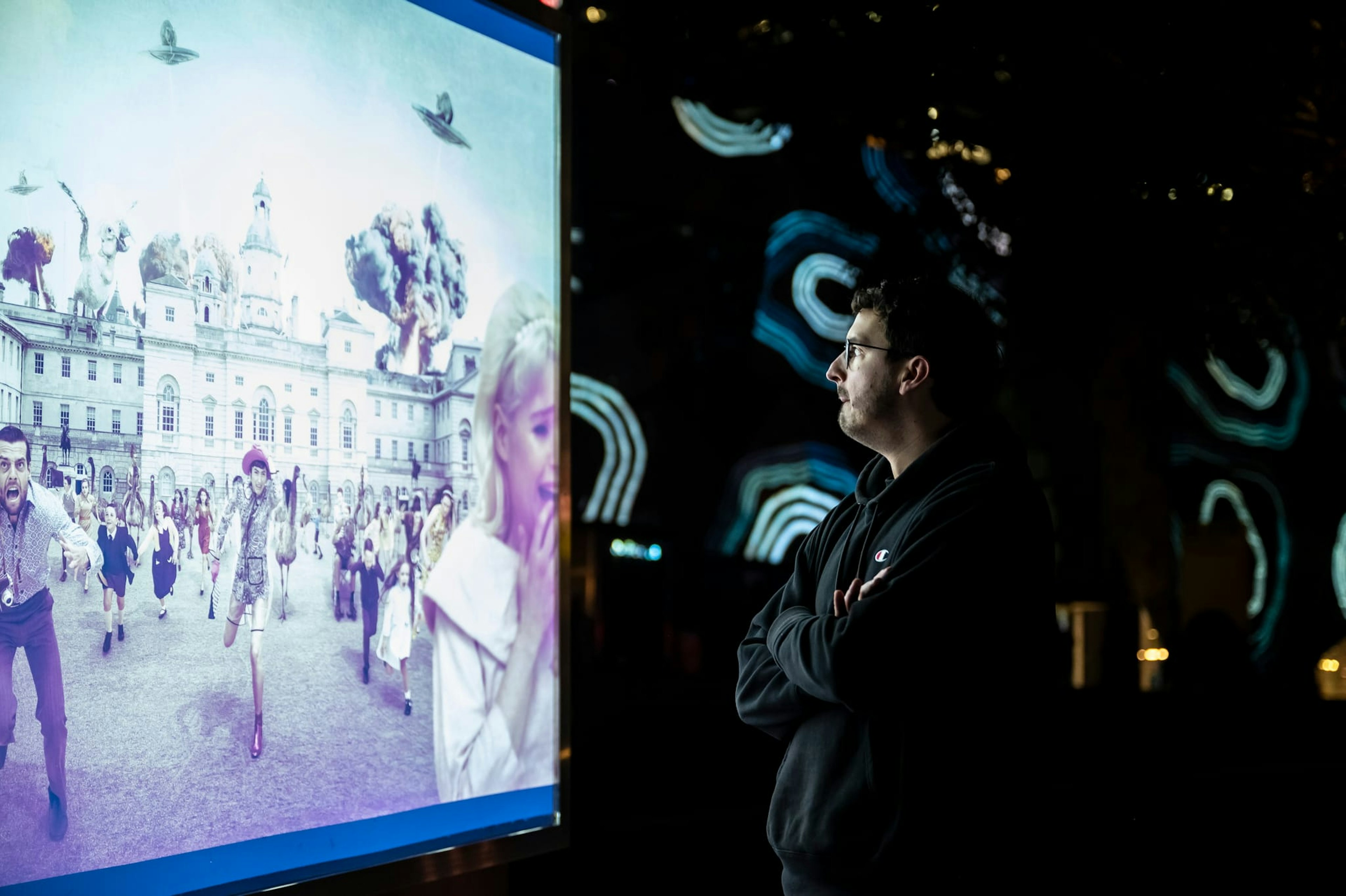 a man looks at an lit up artword of ufos and aliens attacking a street. Behind him, circular projections light up the buildings of Fed Square