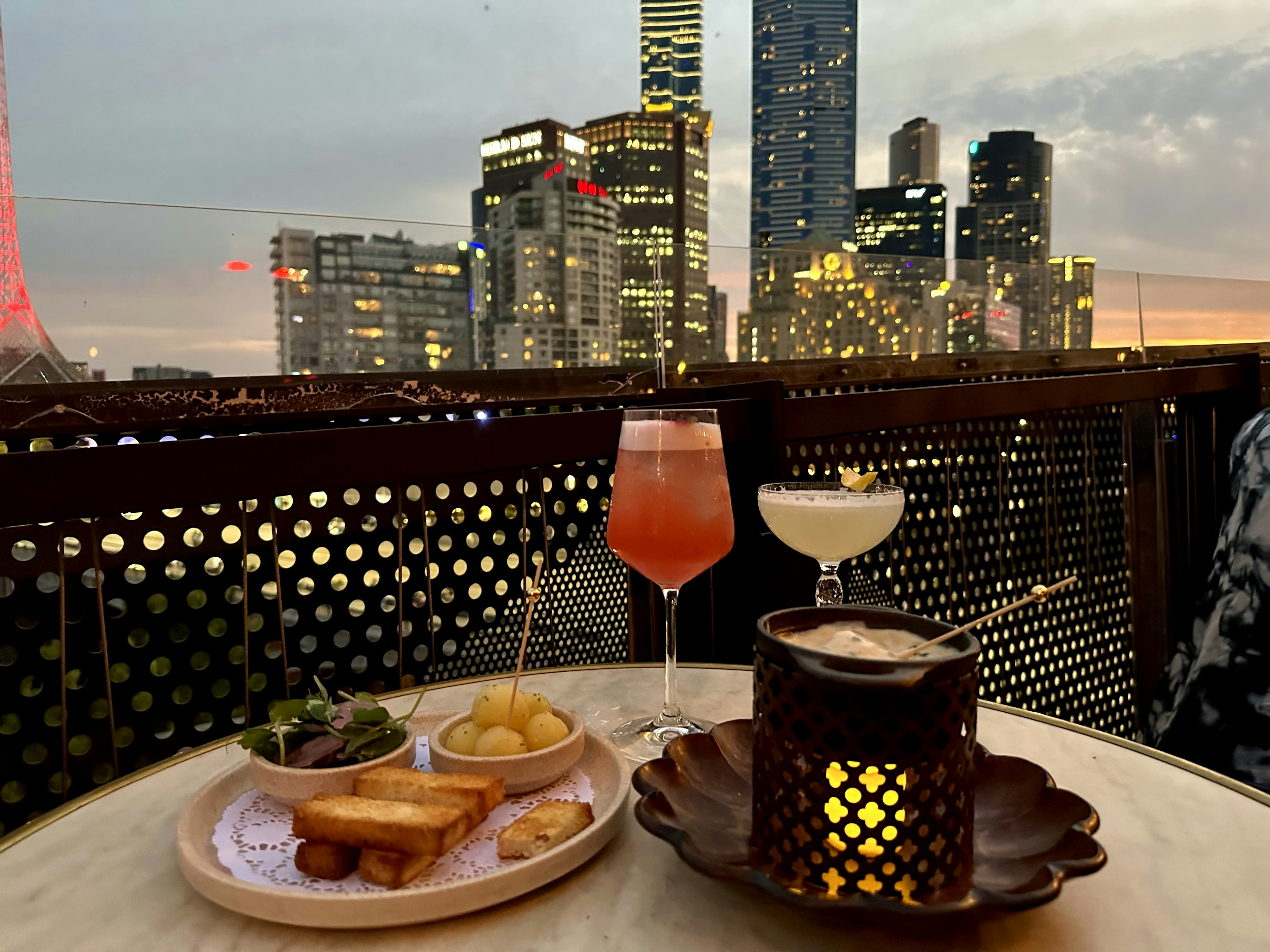 fondue and cocktails on a table, with a view of the city behind